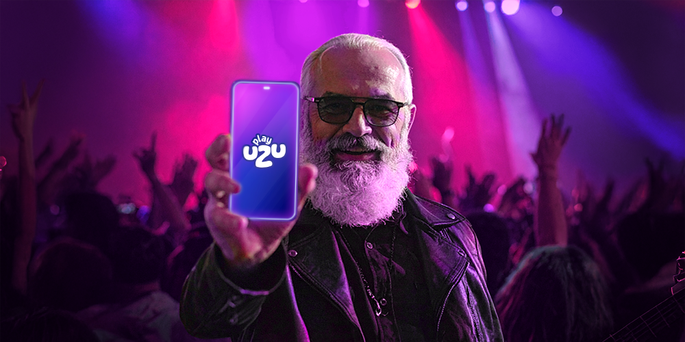 A MAN AROUND 50 YEARS OLD, WHO IS ON STAGE AS IF THE WHOLE CROWD WAS WAITING FOR THE SONG TO START, BUT WHAT HE IS GOING TO START IS PLAYING ON PLAYUZU WITH HIS PHONE IN HAND, SHOWING IT FRONT.